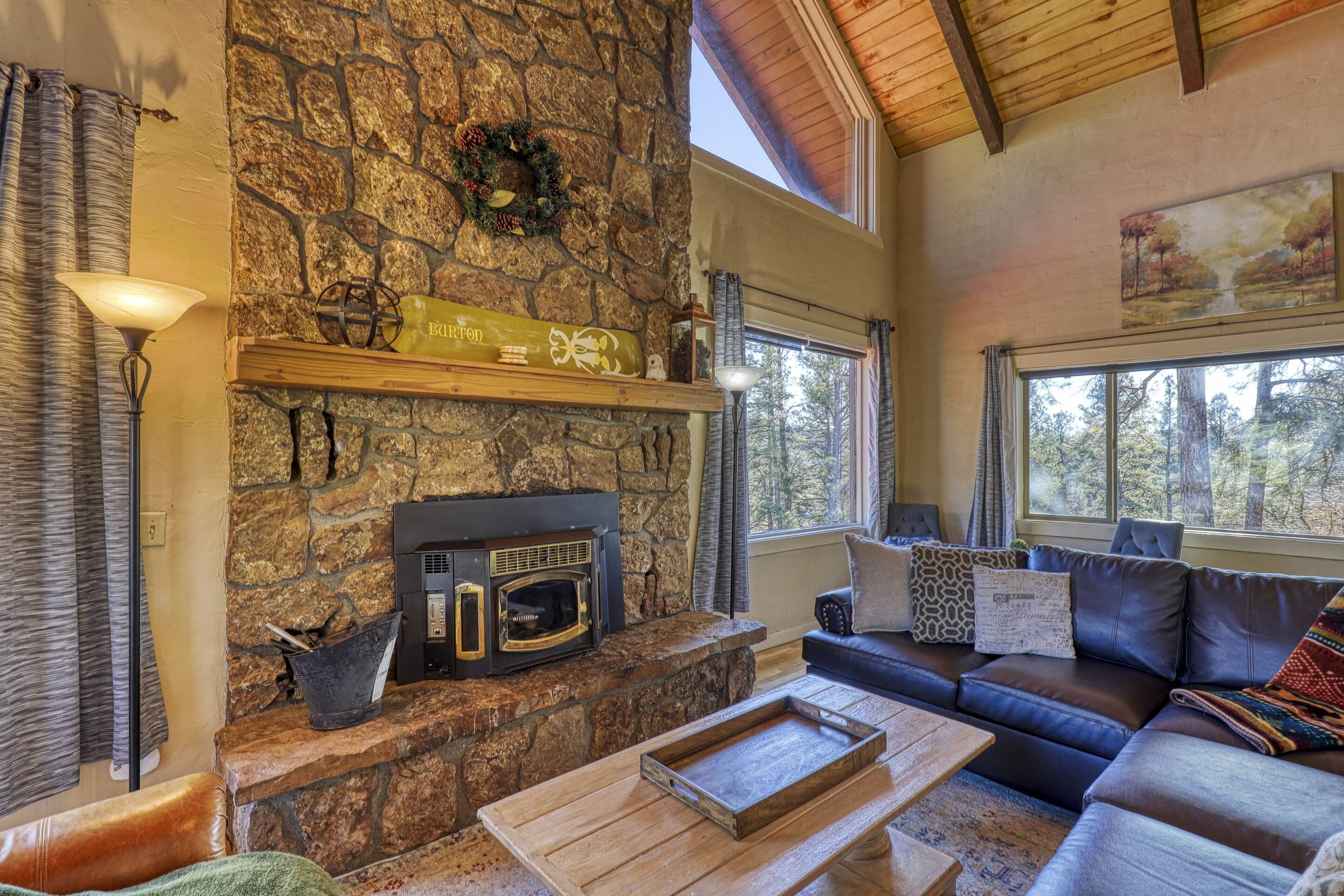 A cozy living room with a stone fireplace, a wooden shelf, a black microwave, a leather sofa, and a large window.