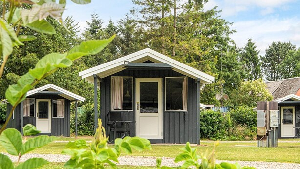 A row of small, dark-colored cabins with white trim, surrounded by lush greenery and trees. - 2 Person Holiday Park Home in Jelling (Jelling)