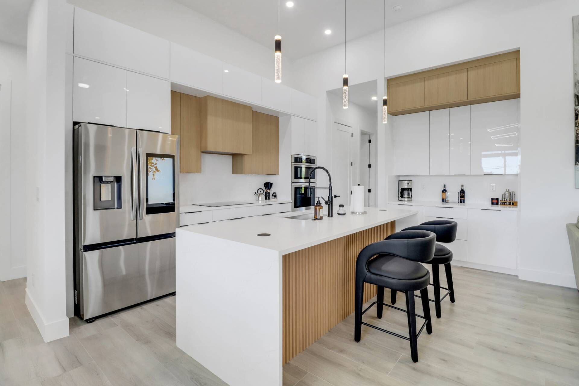 Ett modernt kök med en central köksö, rostfria vitvaror och svarta barstolar.