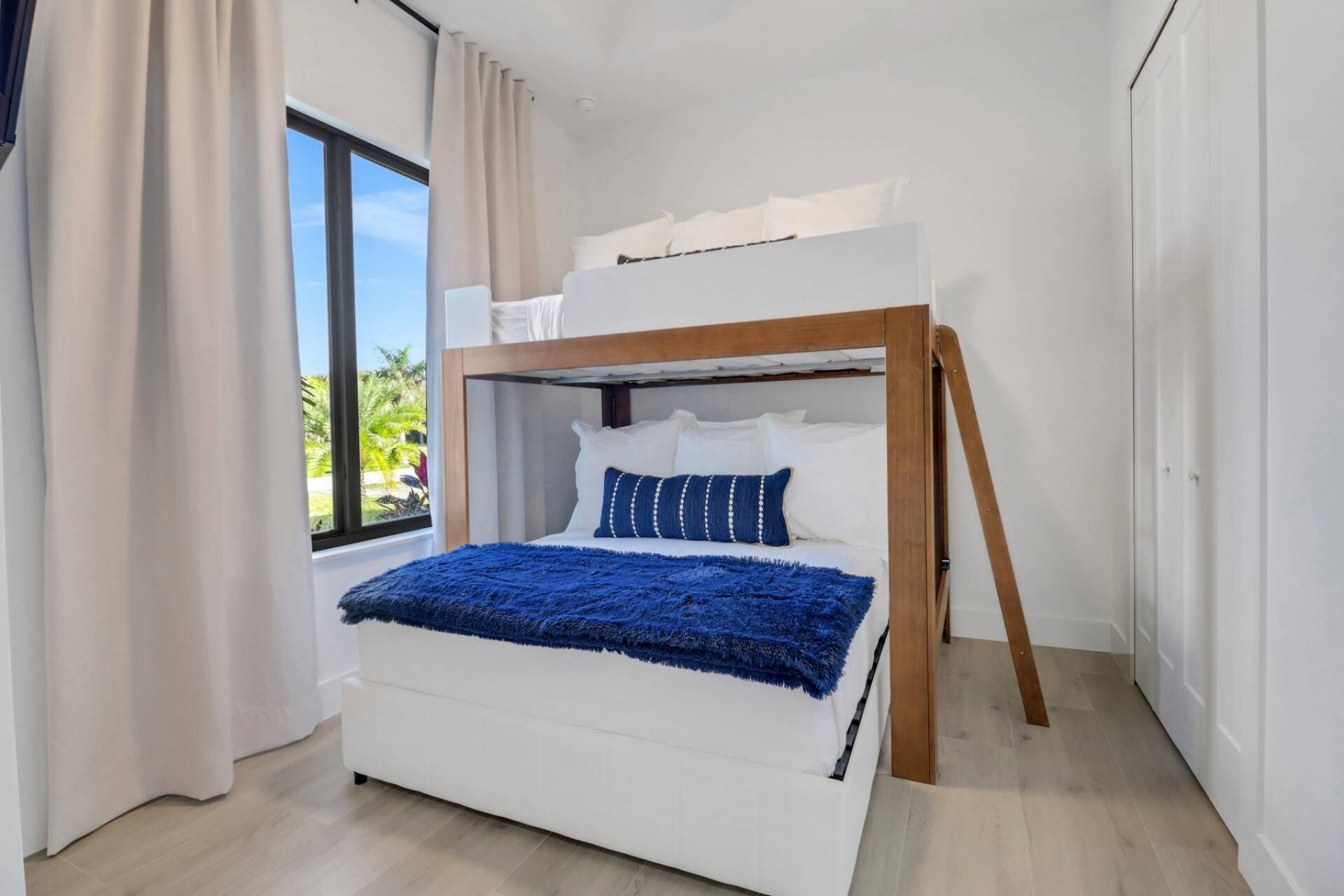 Uma cama de solteiro com estrutura de madeira, roupa de cama branca e um cobertor azul.
