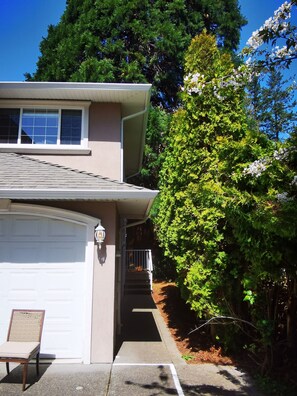 A residential house with a garage, a porch with a chair, and a large tree with white flowers. - Room #B, Eagle's house (Victoria)
