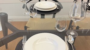 Une table à manger dressée avec des assiettes, des couverts et des verres à vin, entourée de chaises.