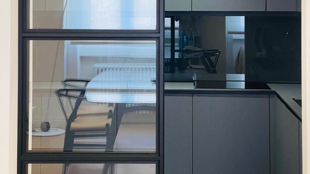 Une cuisine moderne avec des meubles de couleur sombre, un coin repas doté d’une table en verre et une vue sur un escalier.
