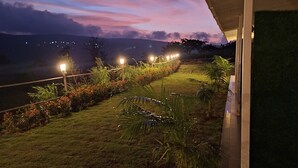A nighttime view of a landscaped area with a pathway, grass, and plants, under a building with a flat roof. - The Breeze Valley (Jaoli)