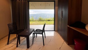 A room with a table and chairs, a wardrobe, and a view of greenery and mountains through a glass door. - The Breeze Valley (Jaoli)