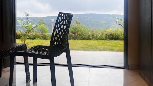 A room with a large sliding glass door leading to a balcony with a view of greenery and hills. - The Breeze Valley (Jaoli)