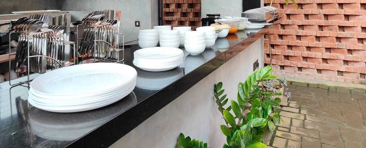 A kitchen counter with stacked plates and utensils, a brick wall, and a potted plant.