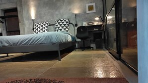 Habitació d'hotel moderna amb un llit, una taula de treball i un ordinador. Hi ha un estotge de benvinguda amb un disseny d'arbre i la paraula "Welcome" escrita a sobre.