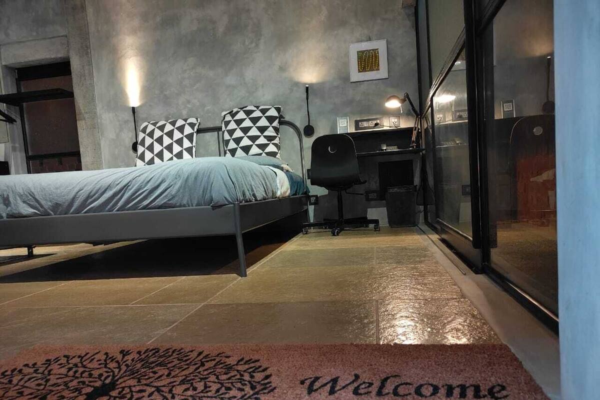 Una habitación de hotel moderna con una cama, un escritorio y una computadora. Hay un tapete de entrada con un diseño de árbol y la palabra 'Welcome'.