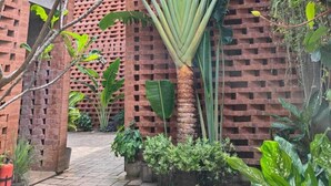Edifici de maó amb una planta central envoltada de vegetació variada.