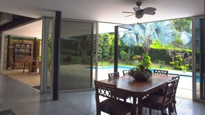 Un espace repas offrant une vue sur une piscine et un jardin tropical.