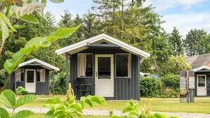 Une rangée de petites cabanes aux couleurs sombres, rehaussées de bordures blanches, entourées d’une végétation luxuriante et d’arbres.
