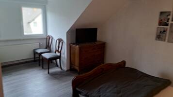 A bedroom with a bed, a wooden dresser, a television on top, two chairs, and a window.