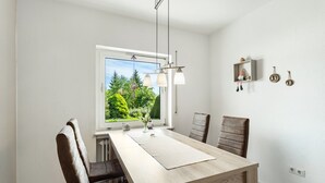 A dining area with a wooden table, chairs, pendant lights, a window with a view of greenery, and a shelf with decorative items. - Holiday Apartment 'Auszeit Sauerland' with Private Terrace and Garden (Meinerzhagen)