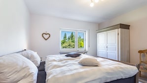 A bedroom with a bed, a window with a view of trees, a wardrobe, and a heart-shaped decoration on the wall. - Holiday Apartment 'Auszeit Sauerland' with Private Terrace and Garden (Meinerzhagen)