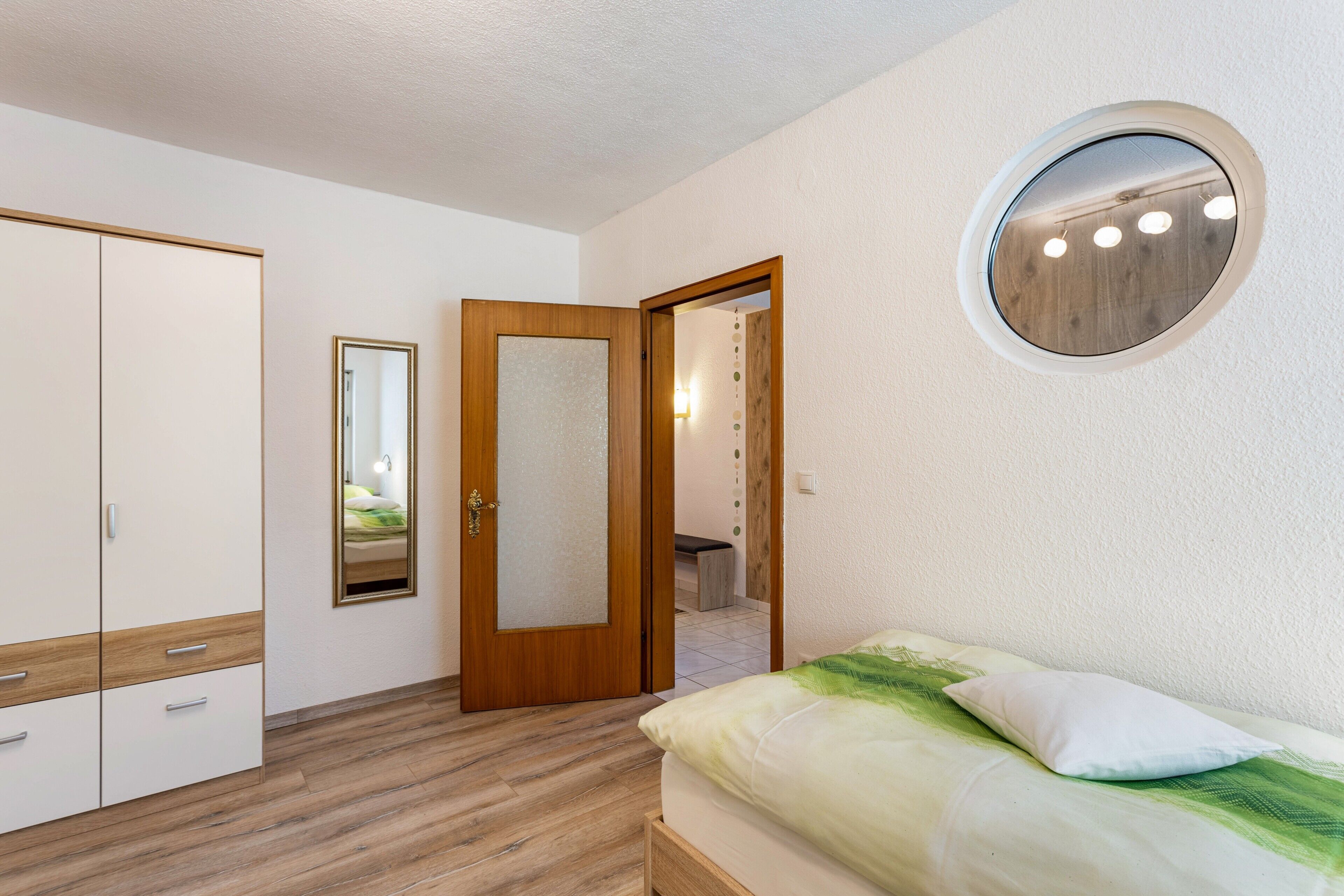 Ein Schlafzimmer mit einem Bett, einem Kleiderschrank, einem Spiegel und einem runden Spiegel an der Wand.