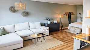 Ein modernes Wohnzimmer mit Sofa, rundem Tisch, Stehlampe und Bett.