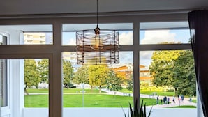 Ein Zimmer mit großem Fenster, einer Pendelleuchte, einem Blumentopf und einer kleinen Skulptur auf dem Fensterbrett.