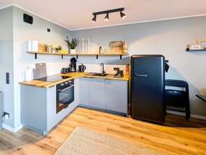 A compact kitchen with a built-in oven, a black refrigerator, and wooden countertops. - Apartment 'Nautilus' in Ferienpark Heiligenhafen (Heiligenhafen)