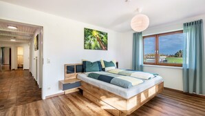 Een slaapkamer met een houten bed, uitzicht op de omgeving, een schilderij aan de muur en een plafondlamp.