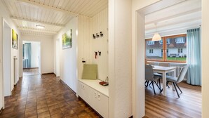 Een gang met een bank, een eetgedeelte met een tafel en stoelen, en uitzicht naar buiten.