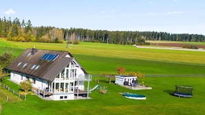 Een huis met een groot terras, een speelplaats en een trampoline in een groen veld.