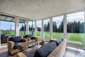 A spacious room with large windows, wicker furniture, and a view of a green landscape. - Holiday apartment 'Naturzeit' with winter garden, balcony and large communal garden (Königsfeld im Schwarzwald)