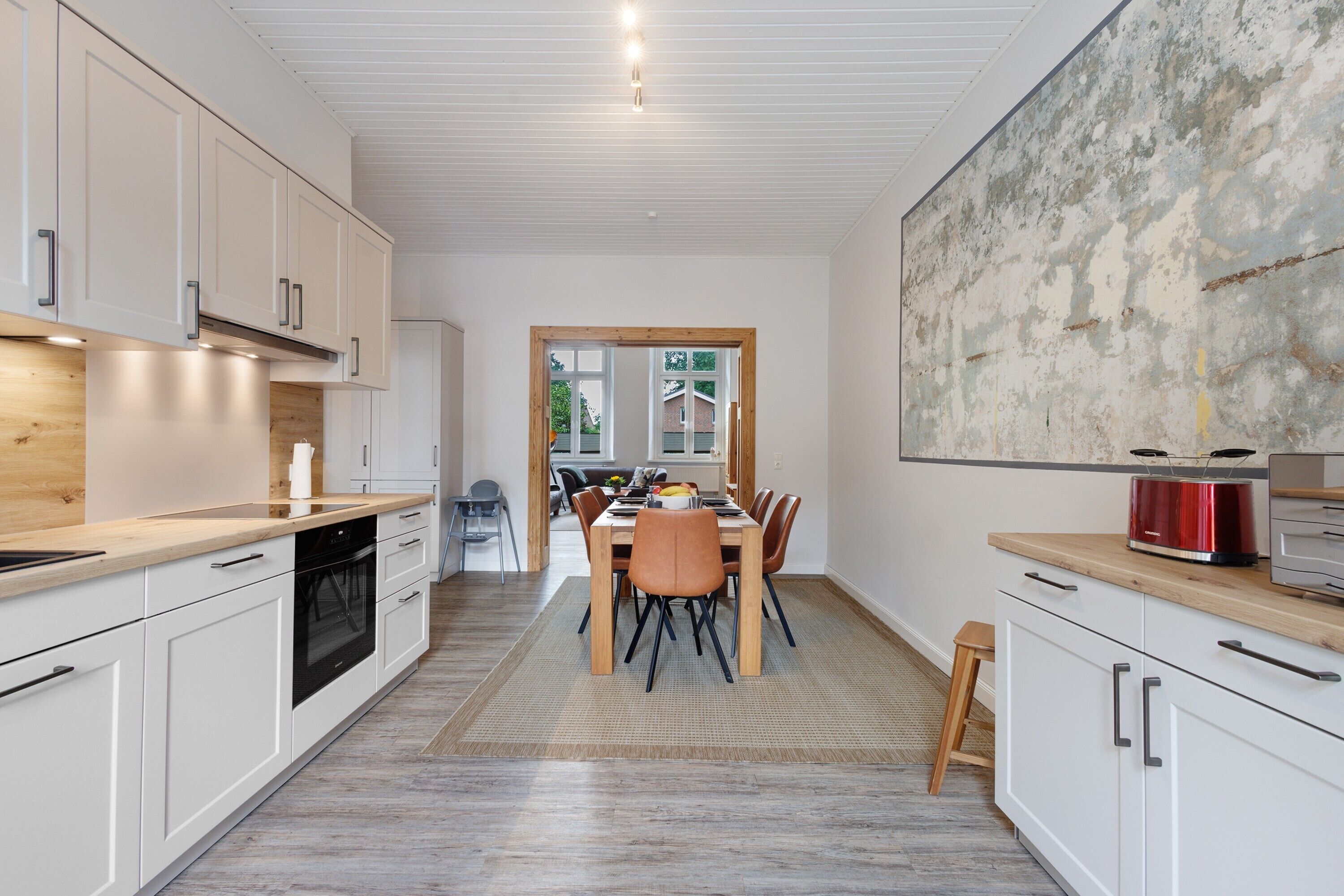 A modern kitchen with white cabinets, a wooden countertop, and a dining area with a table and chairs.