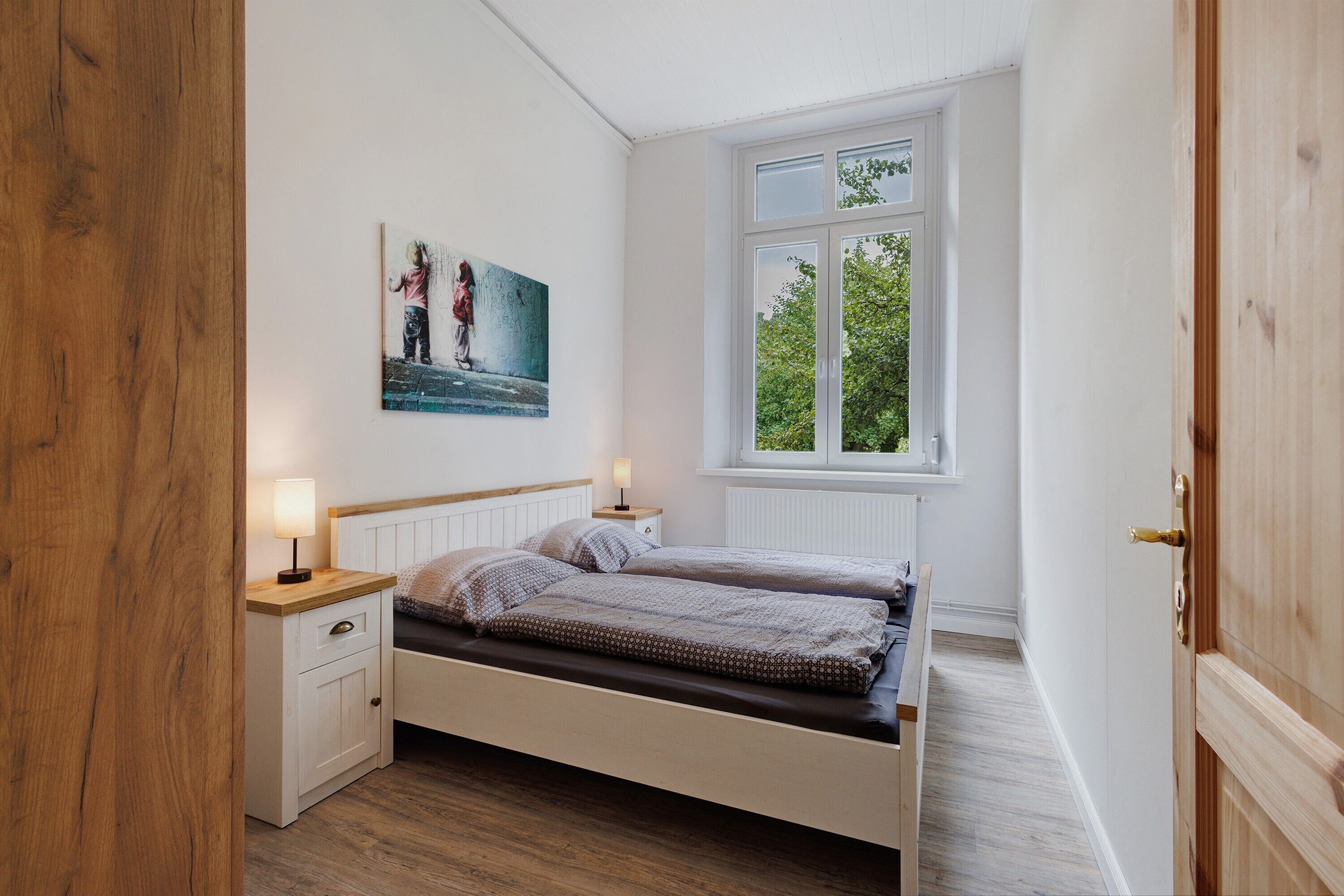 Een slaapkamer met een bed, nachtkastjes, een raam met uitzicht en een schilderij aan de muur.
