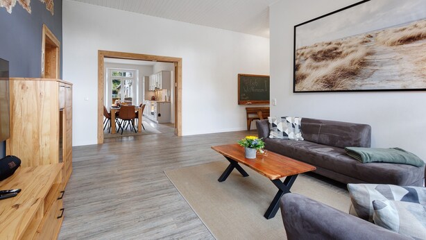 A modern living room with a wooden coffee table, grey sofa, and a large abstract painting. - Apartment 'Reit- Und Ferienhof Alte Dorfschule' with  Private Terrace and Wi-Fi (Holstenniendorf)