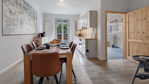 A modern kitchen with white cabinets, a dining area with a wooden table and chairs, and a large abstract painting on the wall. - Apartment 'Reit- Und Ferienhof Alte Dorfschule' with  Private Terrace and Wi-Fi (Holstenniendorf)