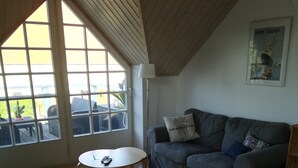 Een kamer met een hoge plafond, een grijze bank, een ronde tafel en een houten stoel.