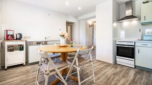 Een moderne keuken met een houten eettafel, witte stoelen, een koffiezetapparaat en een fornuis.