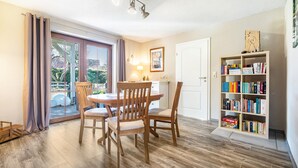 Een eethoek met een tafel en stoelen, een boekenkast en een deur naar een balkon.