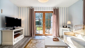 Een woonkamer met een televisie, bank, salontafel en uitzicht door een glazen deur.