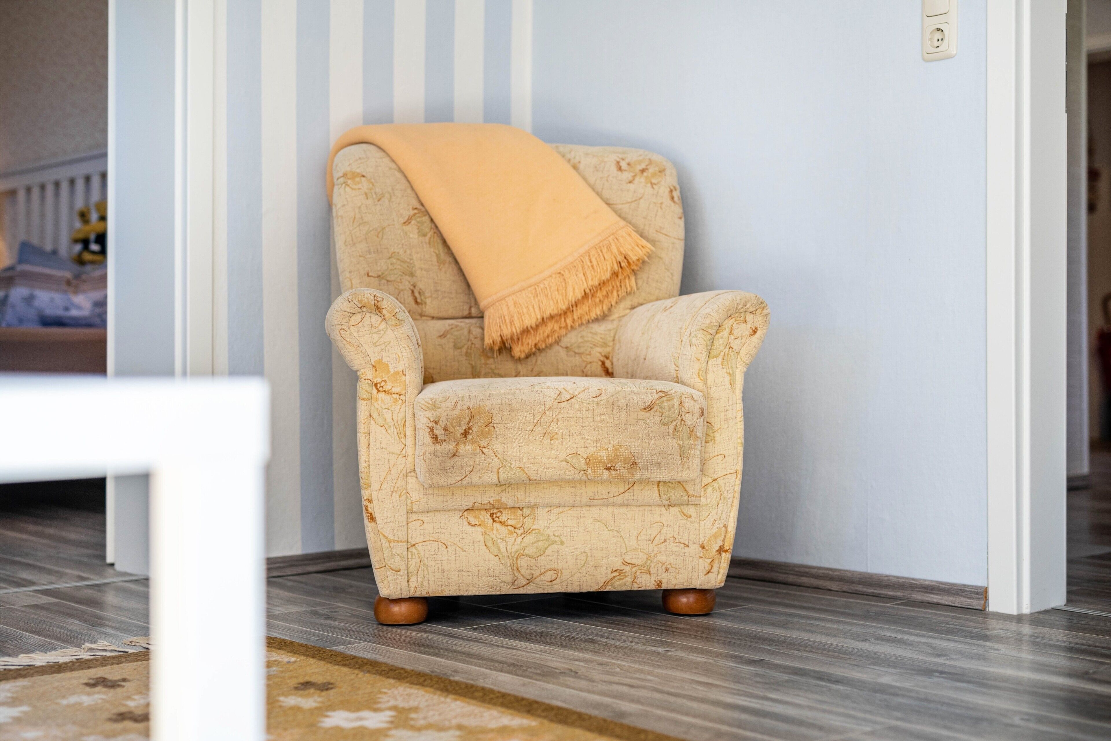 A corner armchair with a floral pattern and a beige throw blanket against a light blue wall.