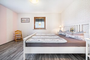 Et soveværelse med seng, en træstol, et natbord, en lampe, et vindue og en væg med blomstermønster.