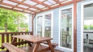 Eine überdachte Terrasse im Freien mit Holztischen und Bänken, eine Glastür, die zu einem Innenbereich führt, und ein Blick auf eine grüne Landschaft.