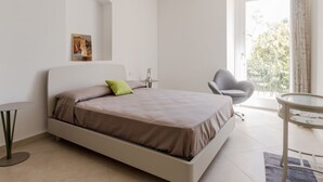 Un dormitorio minimalista con una cama, una silla, una mesita y un cuadro en la pared.