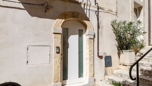 Entrada de edificio con arco de piedra, una puerta, una pequeña planta en maceta y barandilla metálica en los escalones.