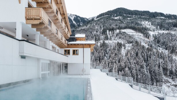 A modern building with a pool, wooden balconies, and a snowy mountain backdrop.