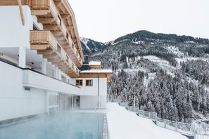 A modern building with a pool, wooden balconies, and a snowy mountain backdrop. - Thurnerhof (Saalbach-Hinterglemm)
