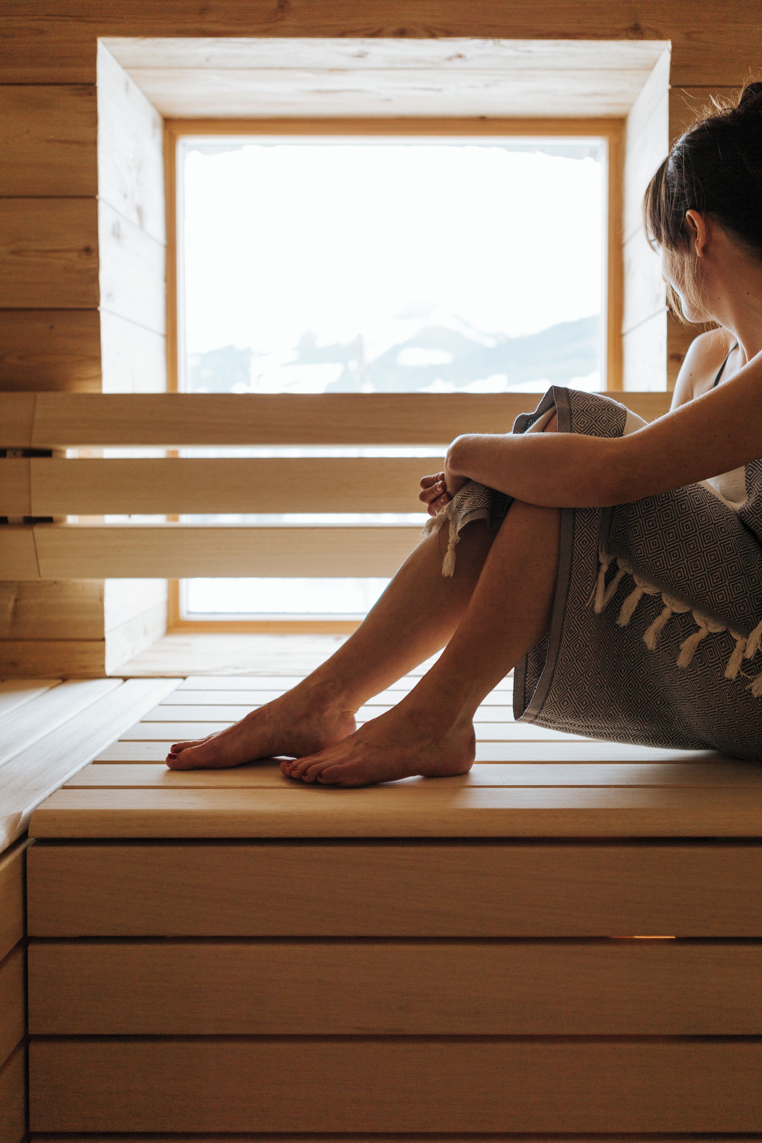 A person sitting on a wooden bench in a room with a wooden interior and a window overlooking a mountainous landscape.