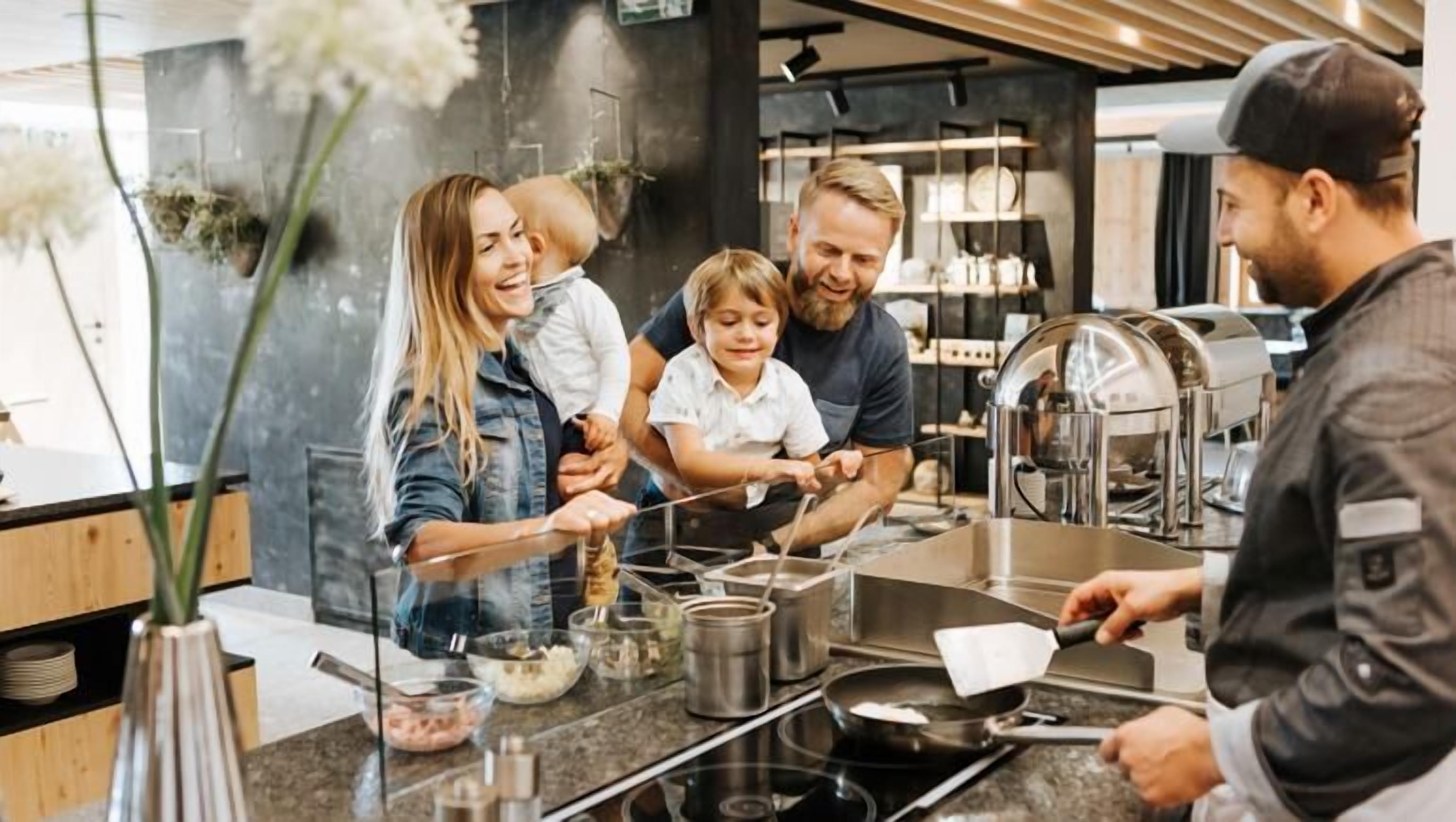 A family cooking together in a modern kitchen with stainless steel appliances and a clear glass barrier.