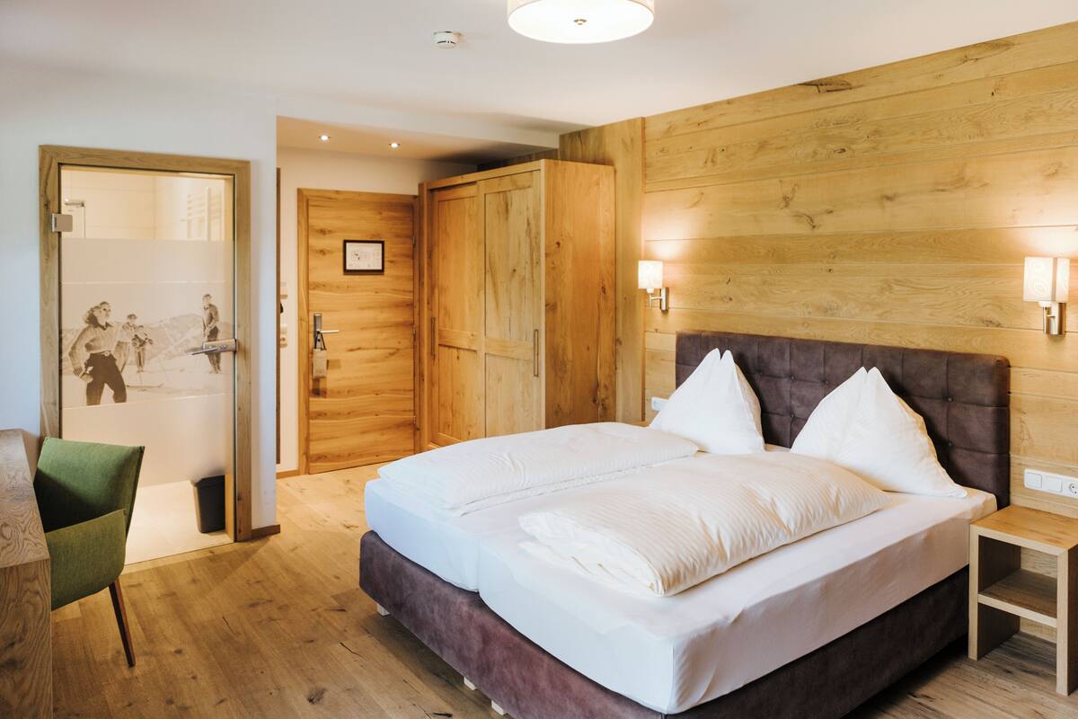 Een slaapkamer met een groot bed, houten paneelwanden, een houten garderobe, een klein nachtkastje en een groene stoel.