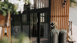 A hotel entrance with a modern design, featuring a glass door, wooden slats, and two potted plants.