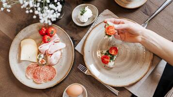 Una mesa servida con platos de queso, jamón, salami y tomates, con una mano escogiendo un tomate.