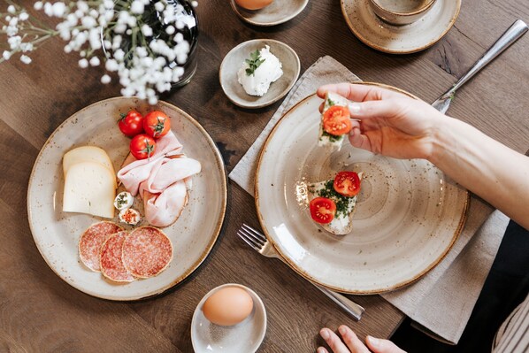 Una mesa servida con platos de queso, jamón, salami y tomates, con una mano escogiendo un tomate.