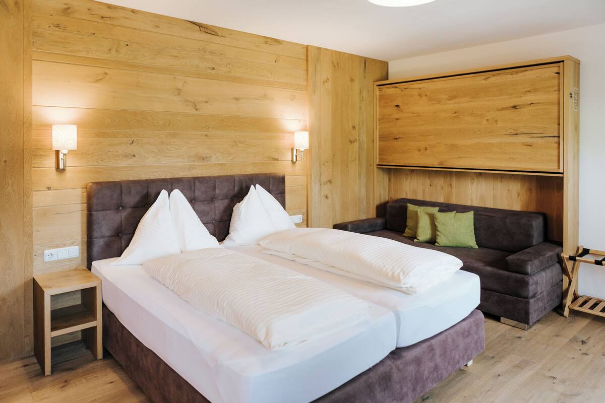 Een slaapkamer met een groot bed, een houten hoofdbord, een nachtkastje, een bank en een aan de muur bevestigde televisie.