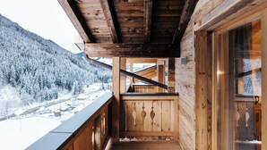 A wooden balcony with a view of a snowy mountain and a village below.